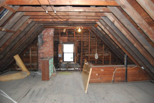 Interior view of an empty attic with exposed beams and window. 